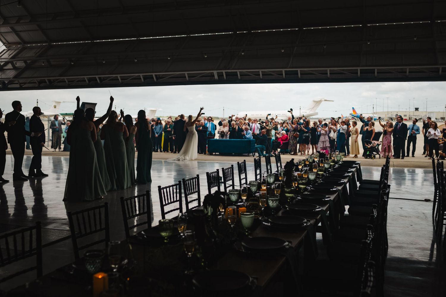 Elegant outdoor wedding reception under a pavilion with guests raising glasses in a toast at a beautifully set dinner table.