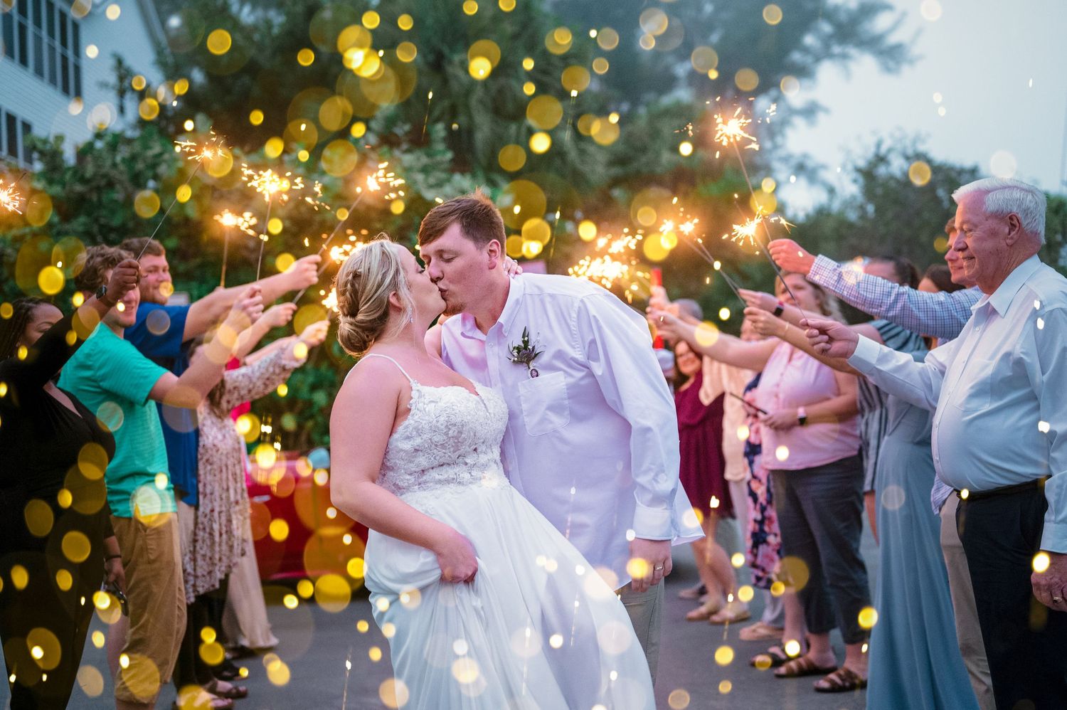 A newlywed couple shares a romantic moment during their sparkler exit at an evening outdoor wedding reception.