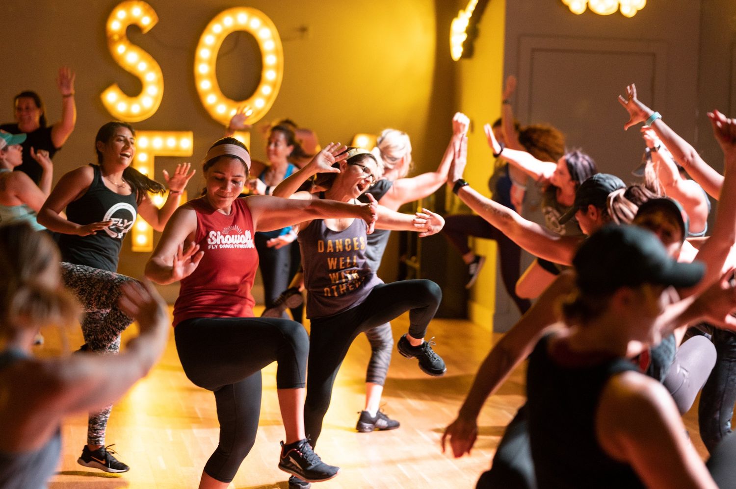Group fitness class participants dancing with enthusiasm under glowing letters.