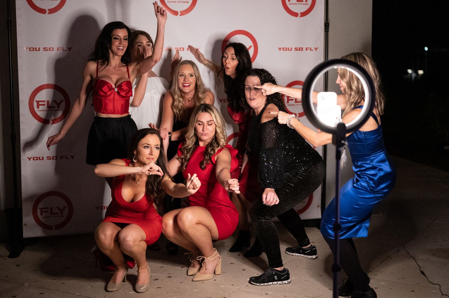 Group striking fun poses at a photo wall with a ring light during an evening event.