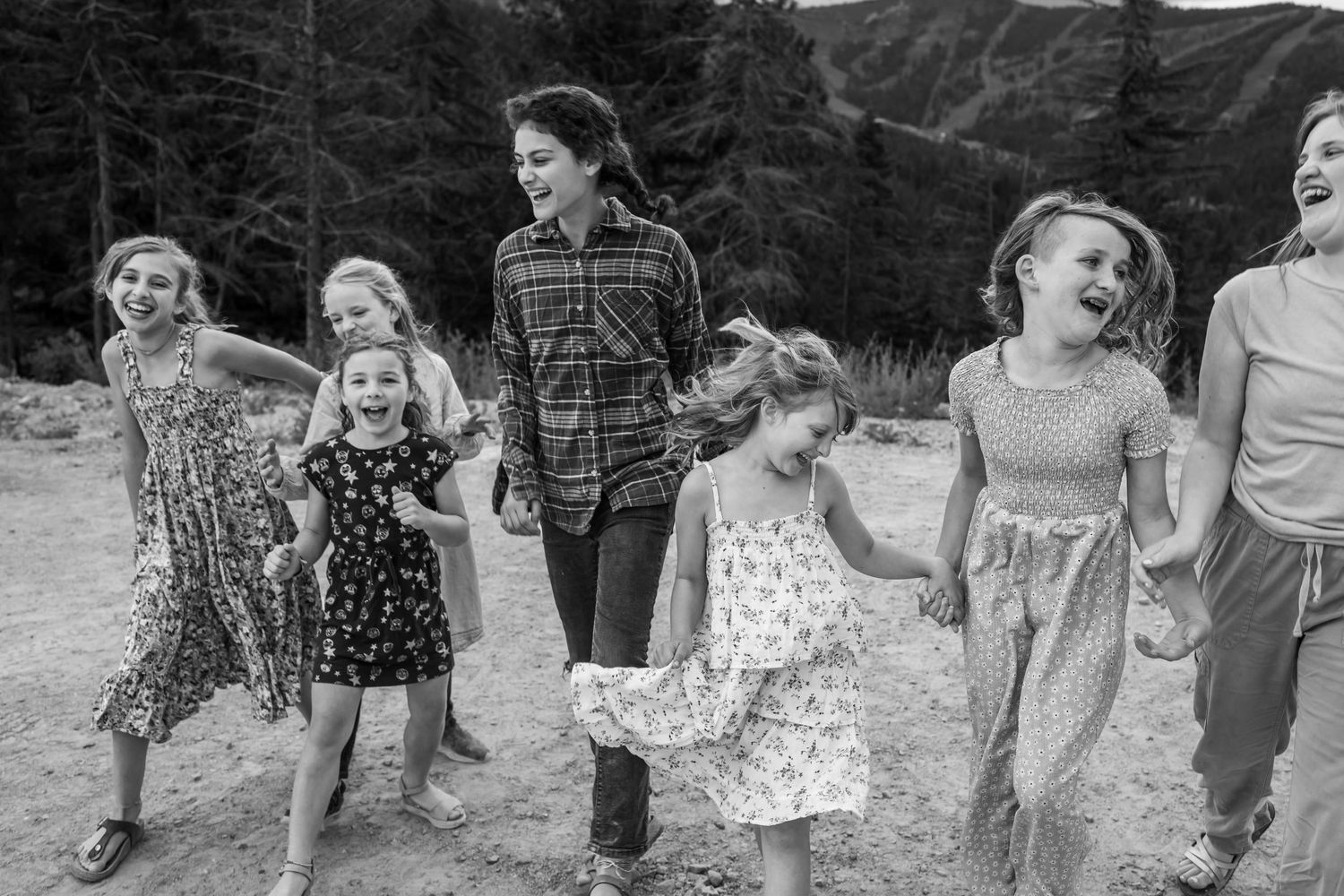 Woman and group of young girls laughing and holding hands outdoors in black and white photo.