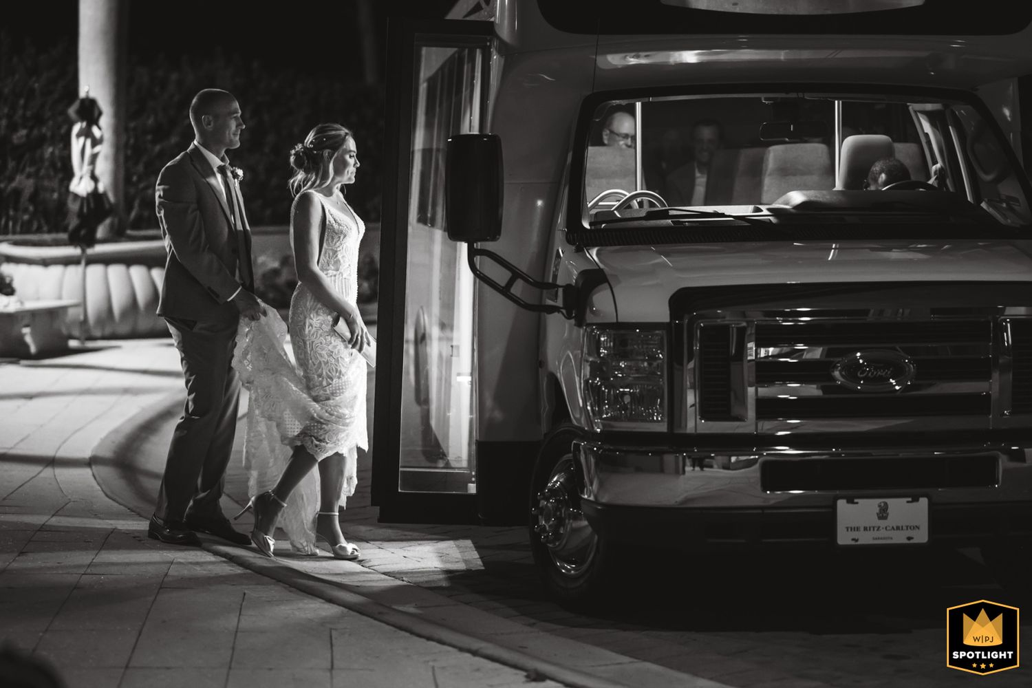 A couple in formal attire exits their wedding celebration at night winning an award for wedding photography in black and white photo.