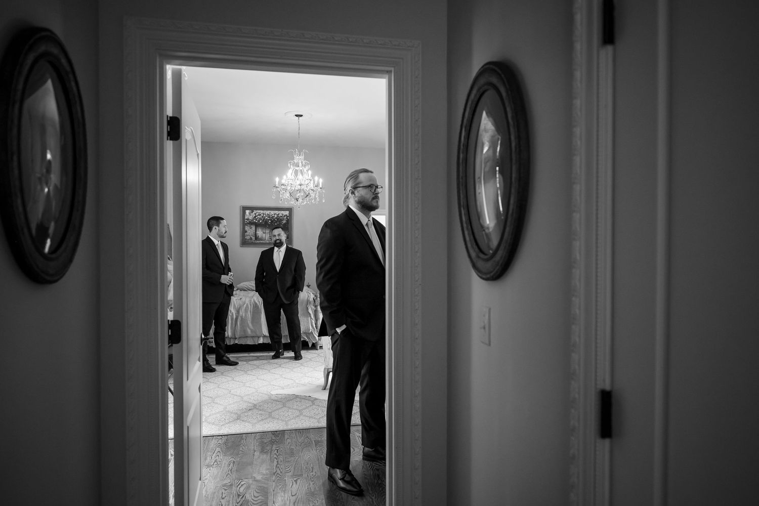 Black and white photograph showing a long hallway with oval-framed portraits on the walls and a chandelier visible at the end.