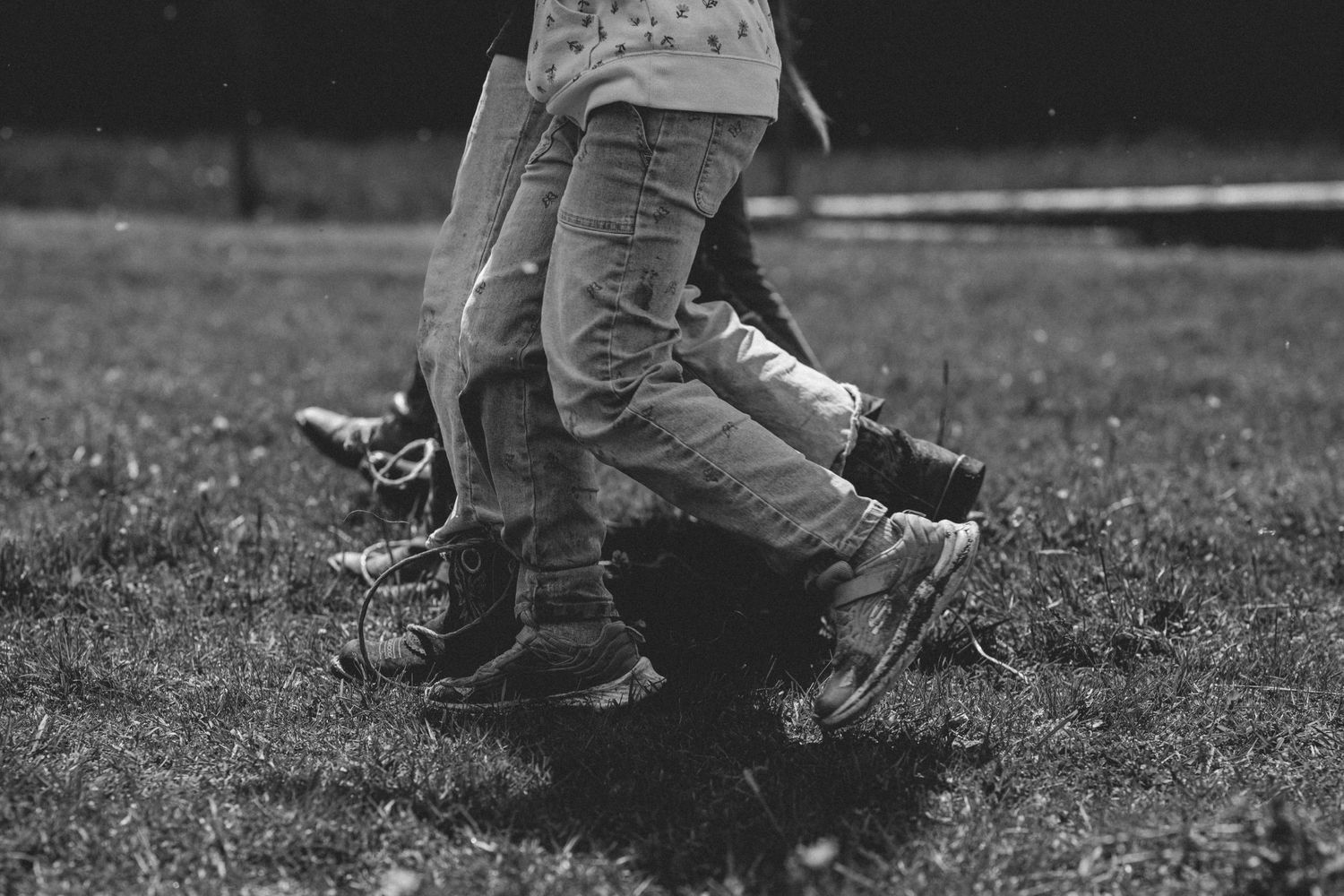 Black and white photo of children's legs in jeans and sneakers playing outdoors on grass.