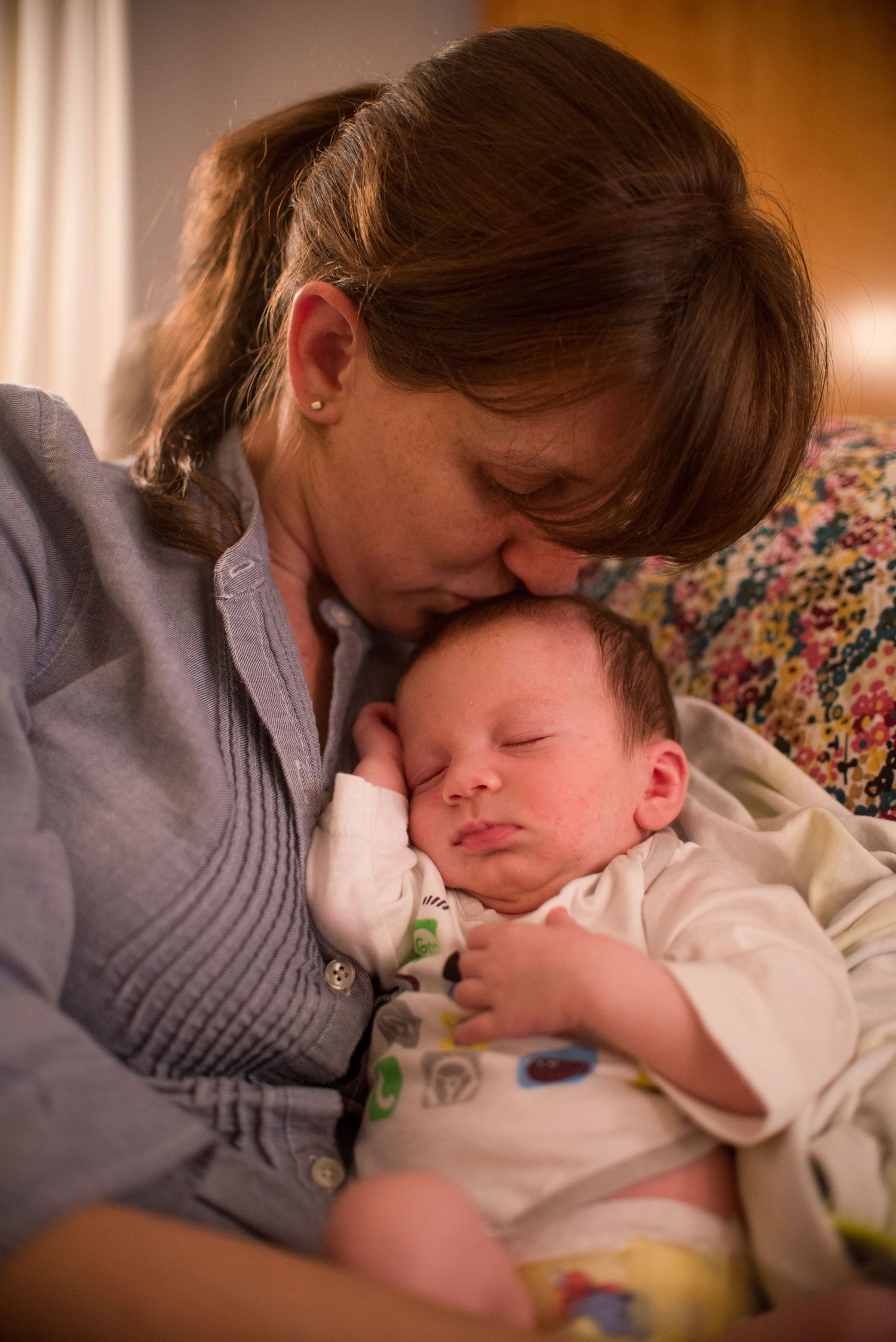 A tender moment shows a sleeping infant being gently cradled and kissed in warm lighting.