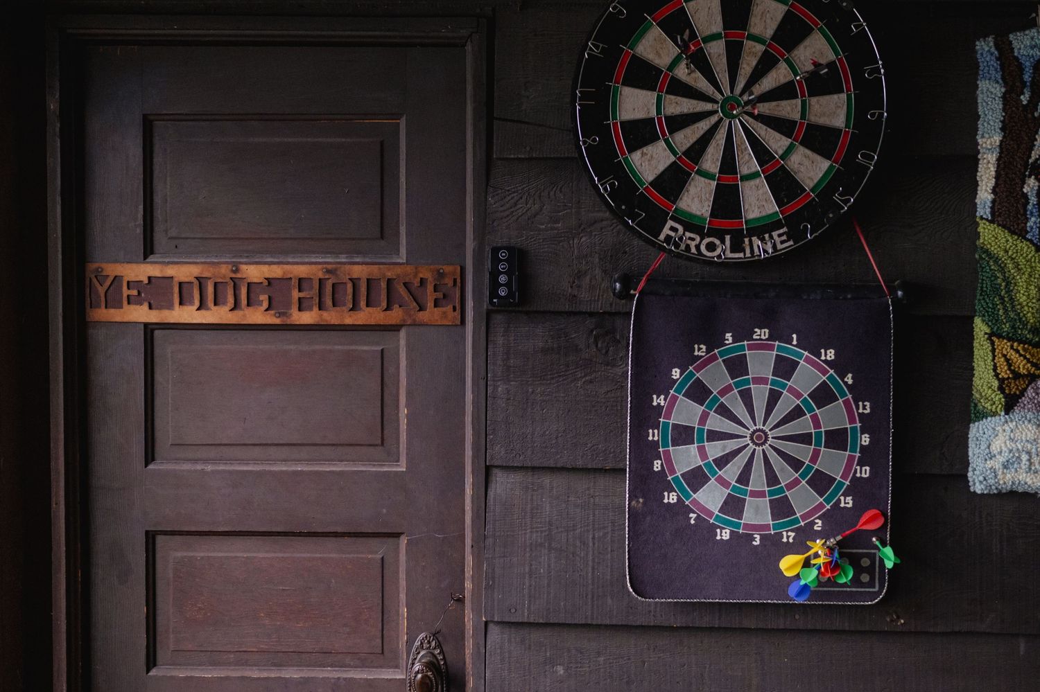 Two dartboards hang on a dark wooden wall next to a door with a decorative wooden sign in a game room.