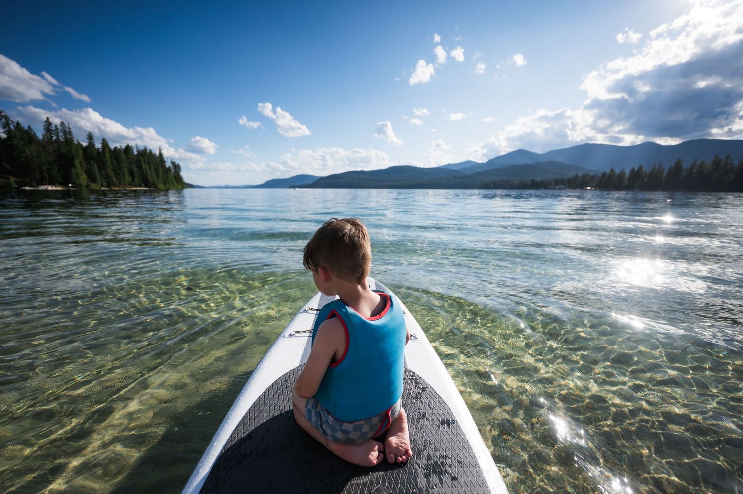 Crystal clear mountain lake waters sparkle under bright sunlight with scenic forested shores in the background.