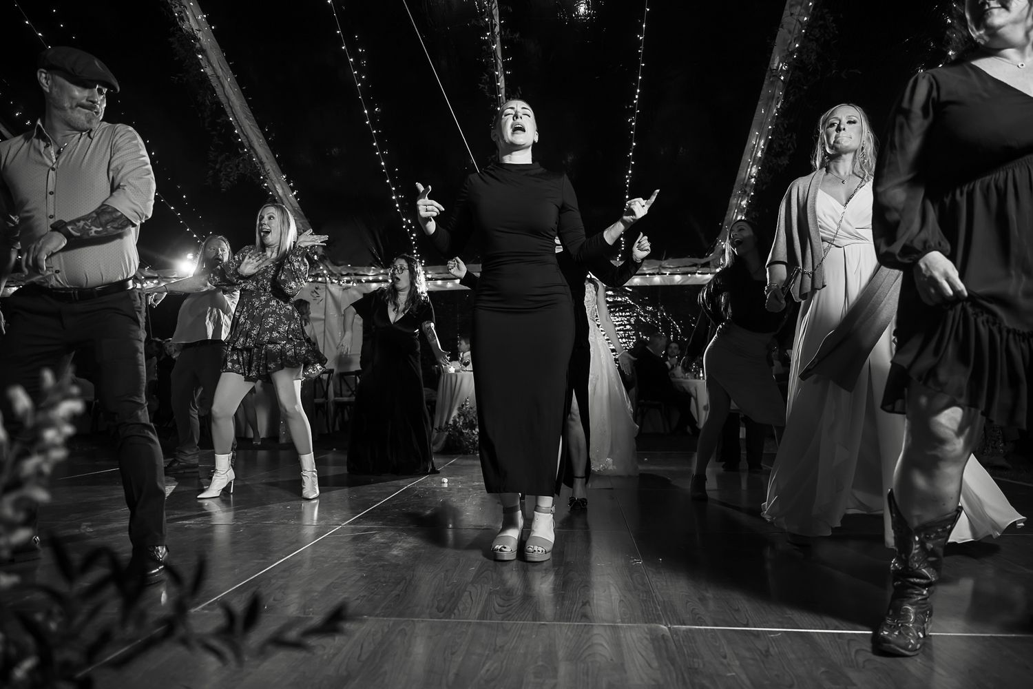 Black and white photo of people dancing at a celebration on a dance floor with dramatic lighting and shadows.