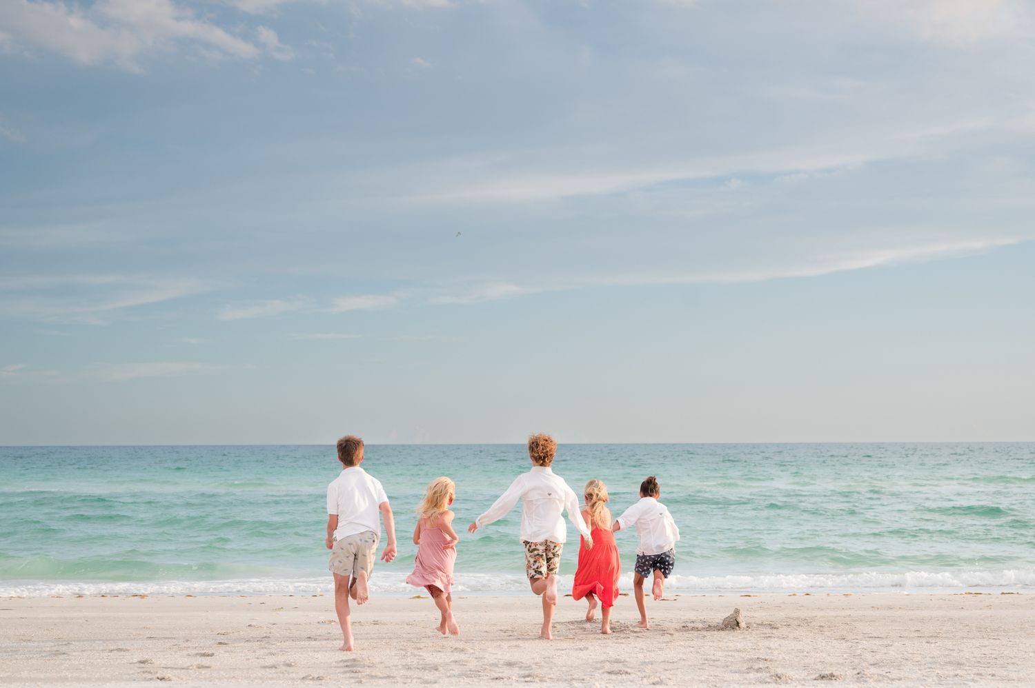 A group of people walk along a scenic beach shoreline with white sand and turquoise waters.
