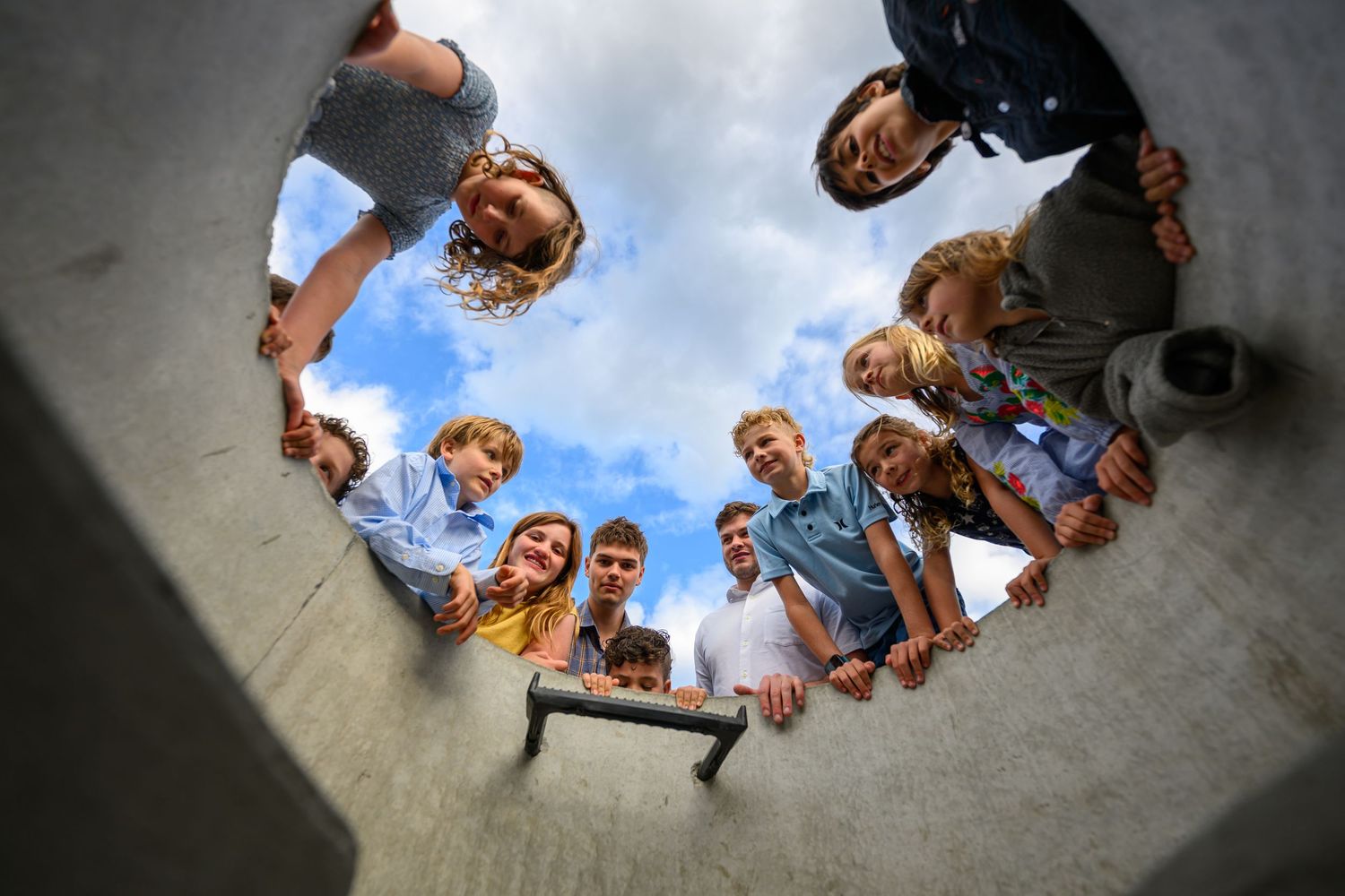 Group of young people forming a circle viewed from below against a blue cloudy sky.