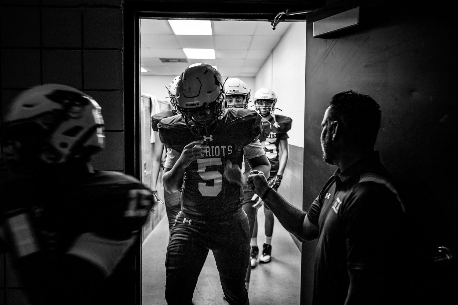 Black and white photo of football players in Patriots uniforms gathered in a tunnel before a game.