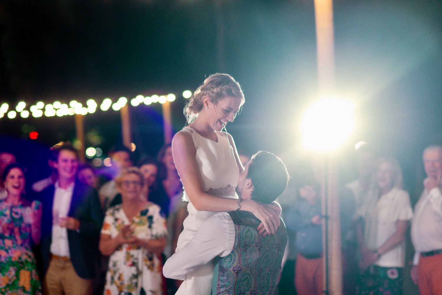 Couples dancing together at a dimly lit wedding reception with string lights glowing overhead.