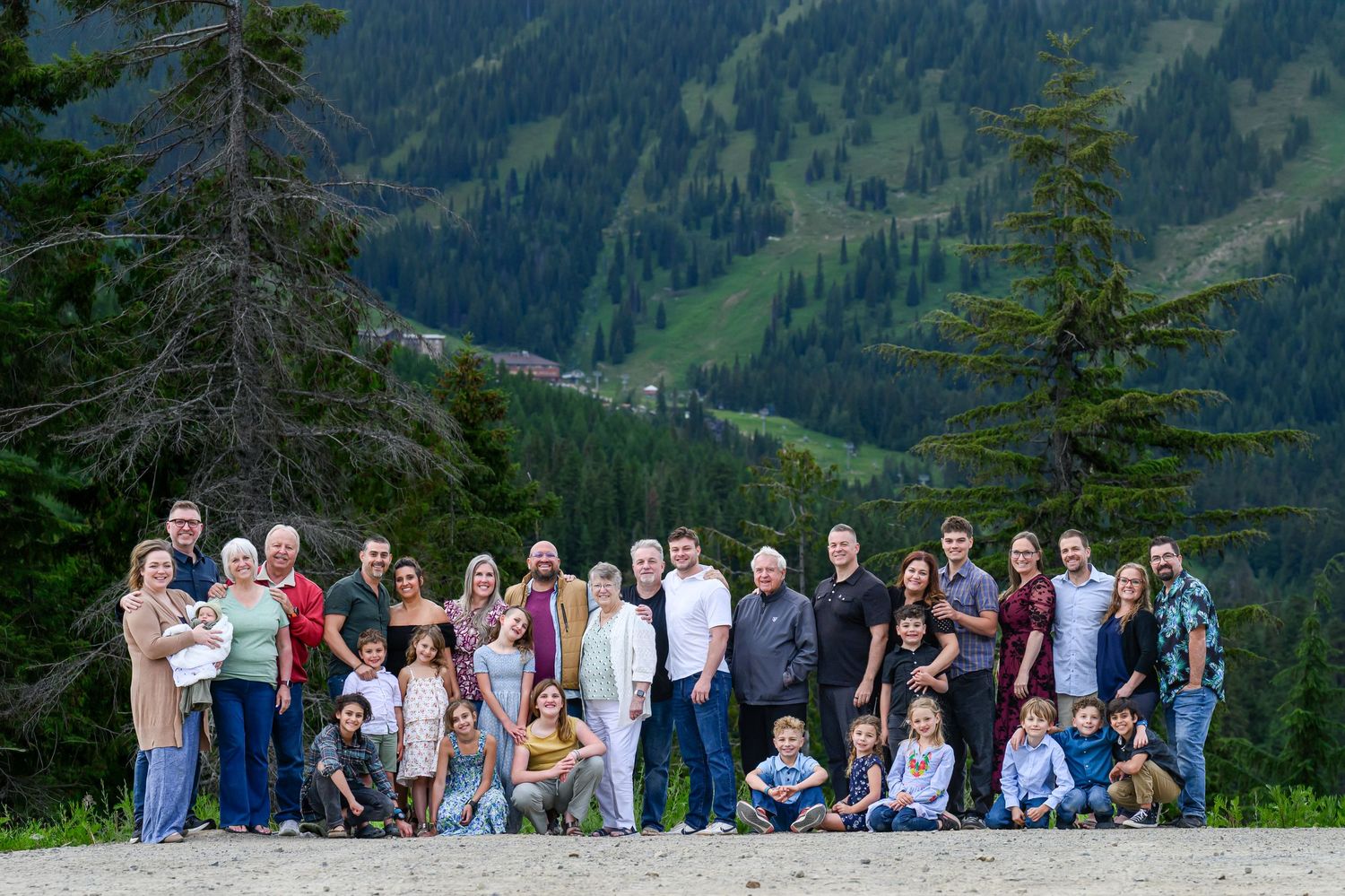Large extended family group photo outdoors with scenic mountain valley and pine trees backdrop.