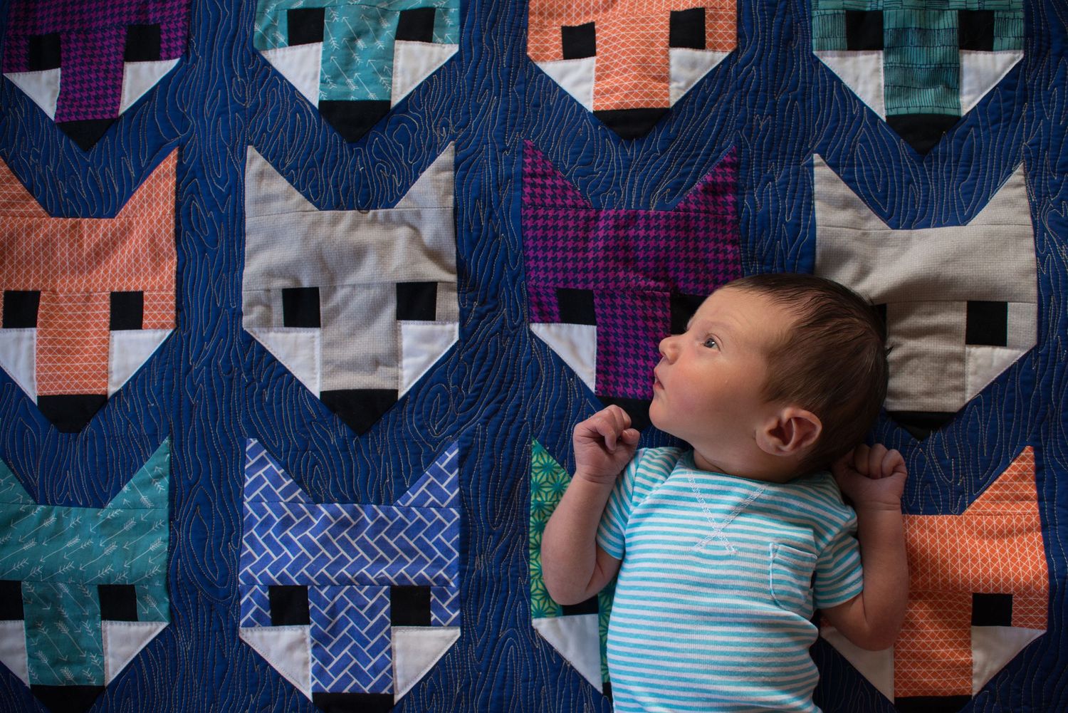 Baby sleeping on colorful patchwork quilt with geometric pattern design.