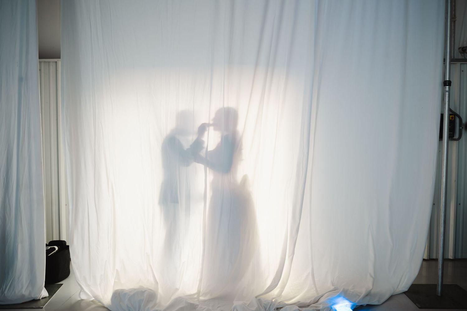 Romantic silhouette of bride and groom kissing behind sheer white curtain at wedding.
