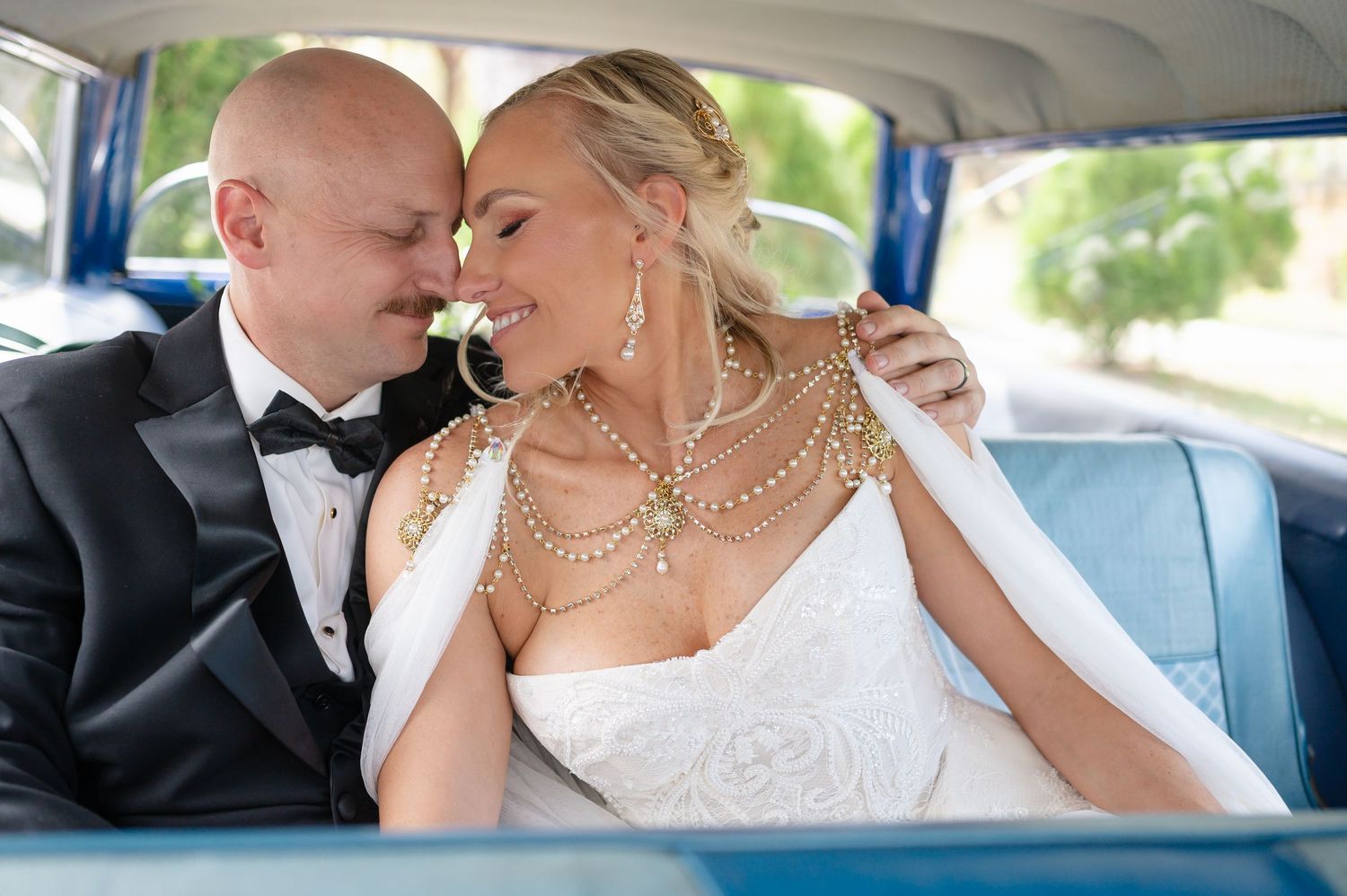 Bride and groom share romantic moment in vintage blue car after wedding ceremony.
