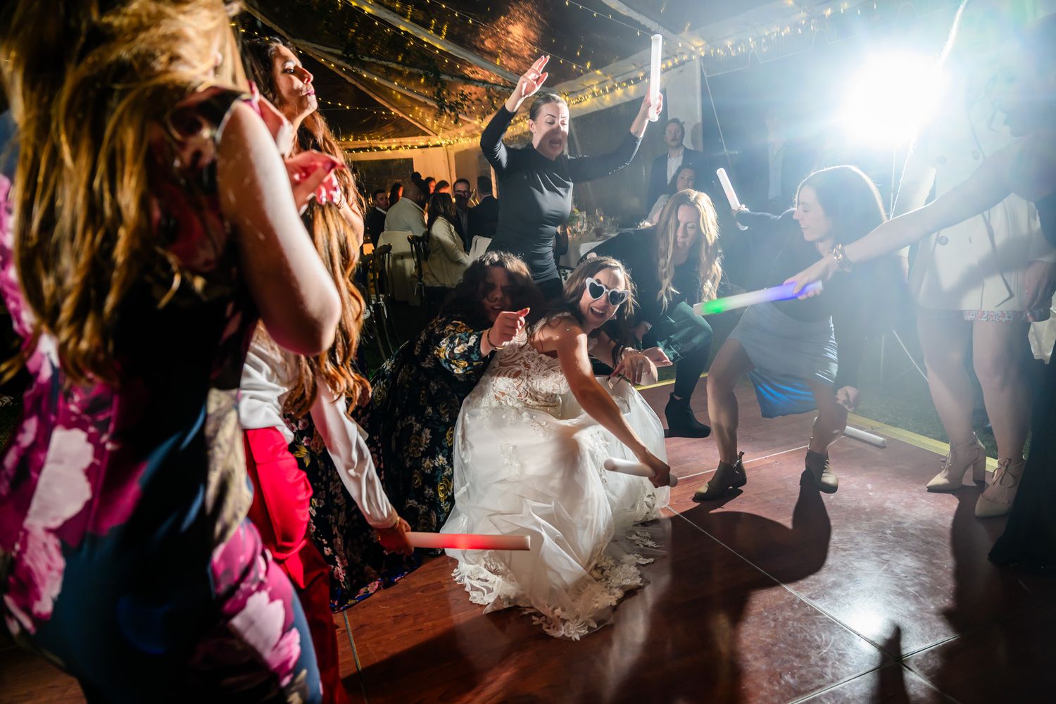 Wedding guests dance and celebrate on a dimly lit dance floor with dramatic lighting effects at an evening reception.