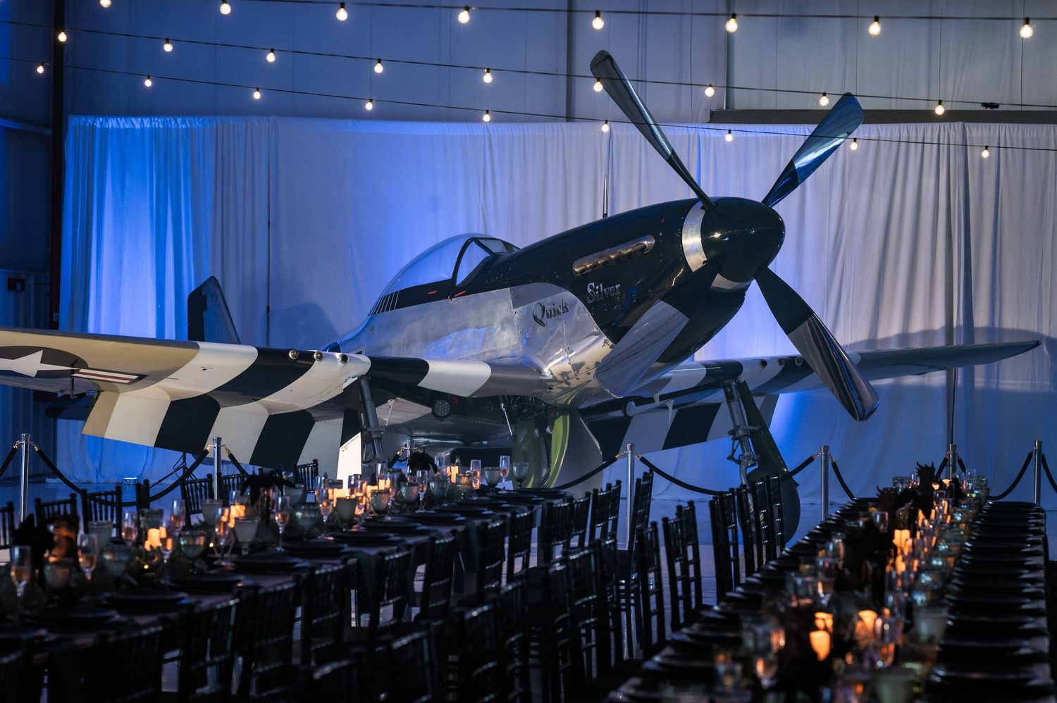 Elegant event venue featuring a vintage WWII fighter plane display with candlelit dining tables.