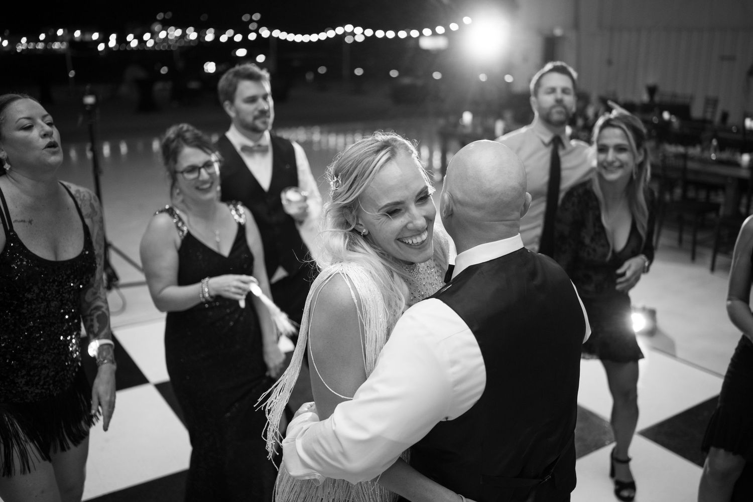 Black and white photo of bride laughing joyfully while dancing with groom at wedding reception.