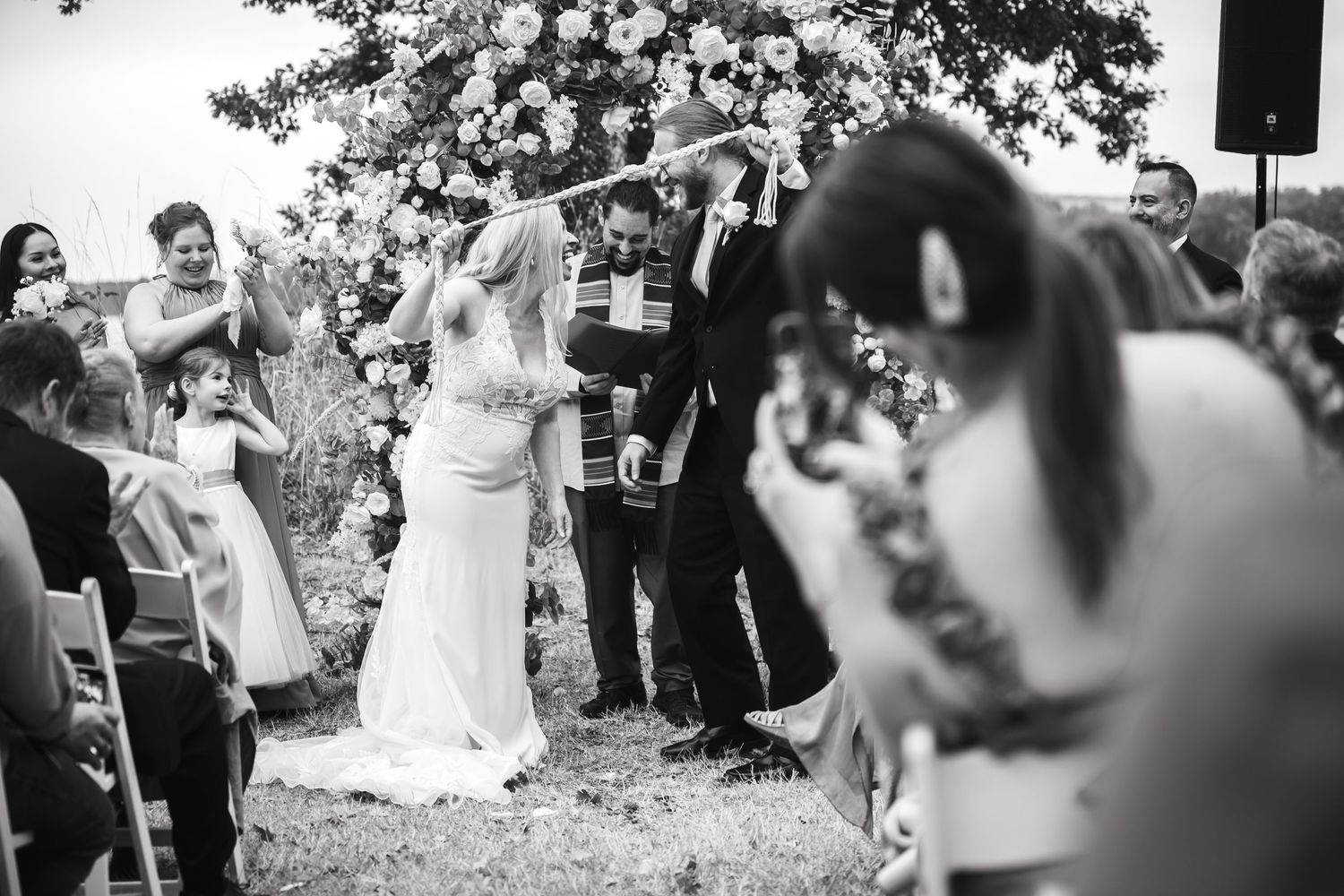 Wedding guests celebrate outdoors under trees during a joyful reception ceremony.