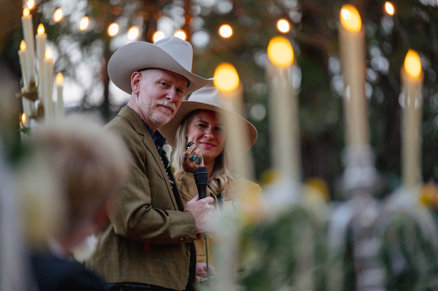 Couple in matching cowboy hats sharing a tender moment at a candlelit outdoor evening reception.