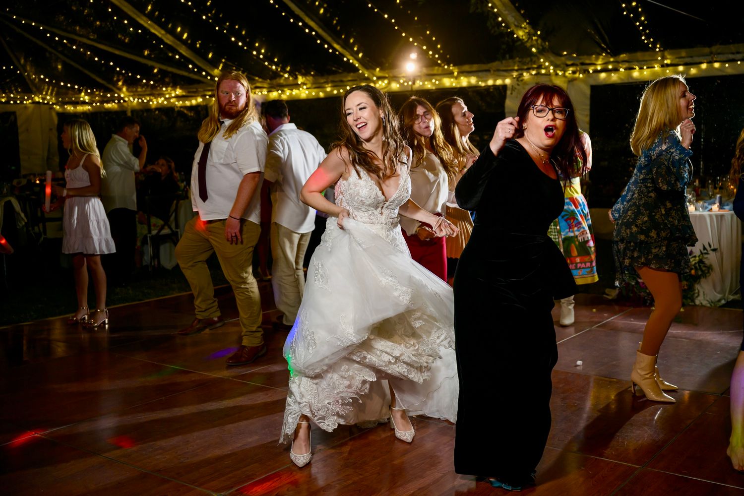 Wedding guests dancing and celebrating on a dance floor decorated with string lights at a reception party.