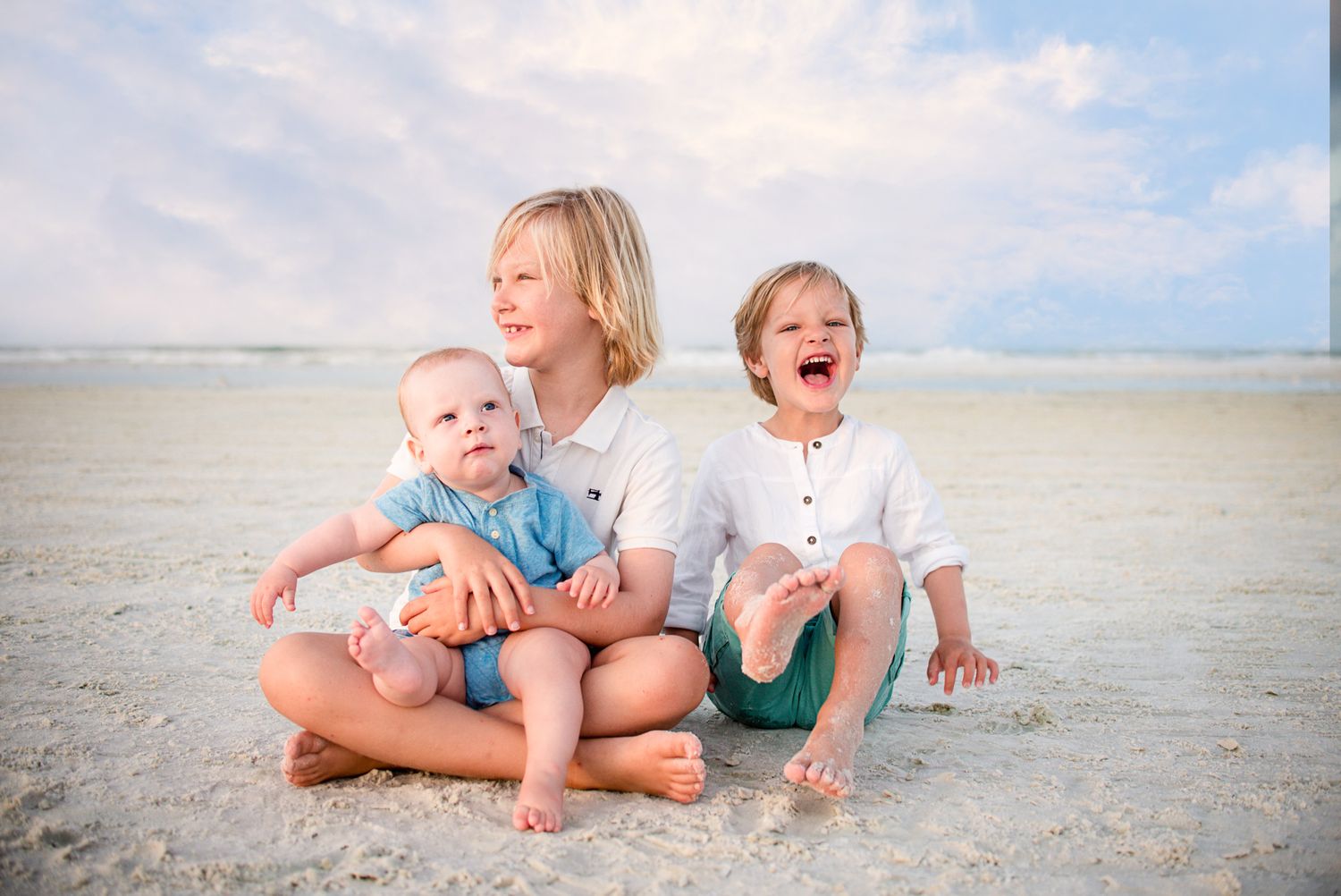 Children playing together on white sandy beach under blue sky.