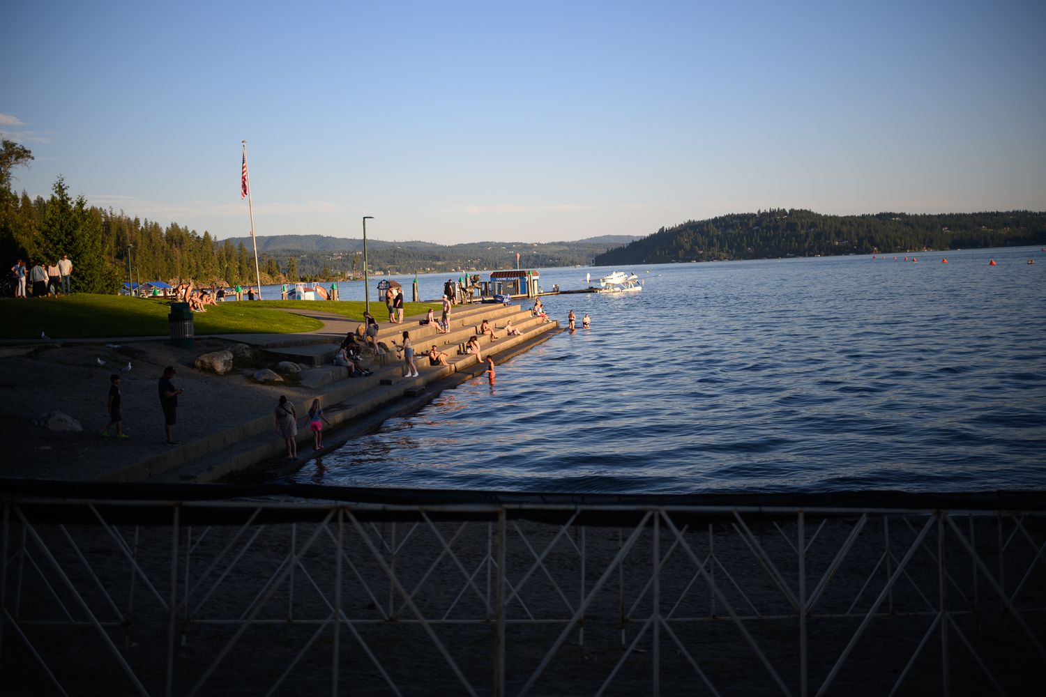 Scenic view of a lakeside dock with swimmers and mountains in the background.