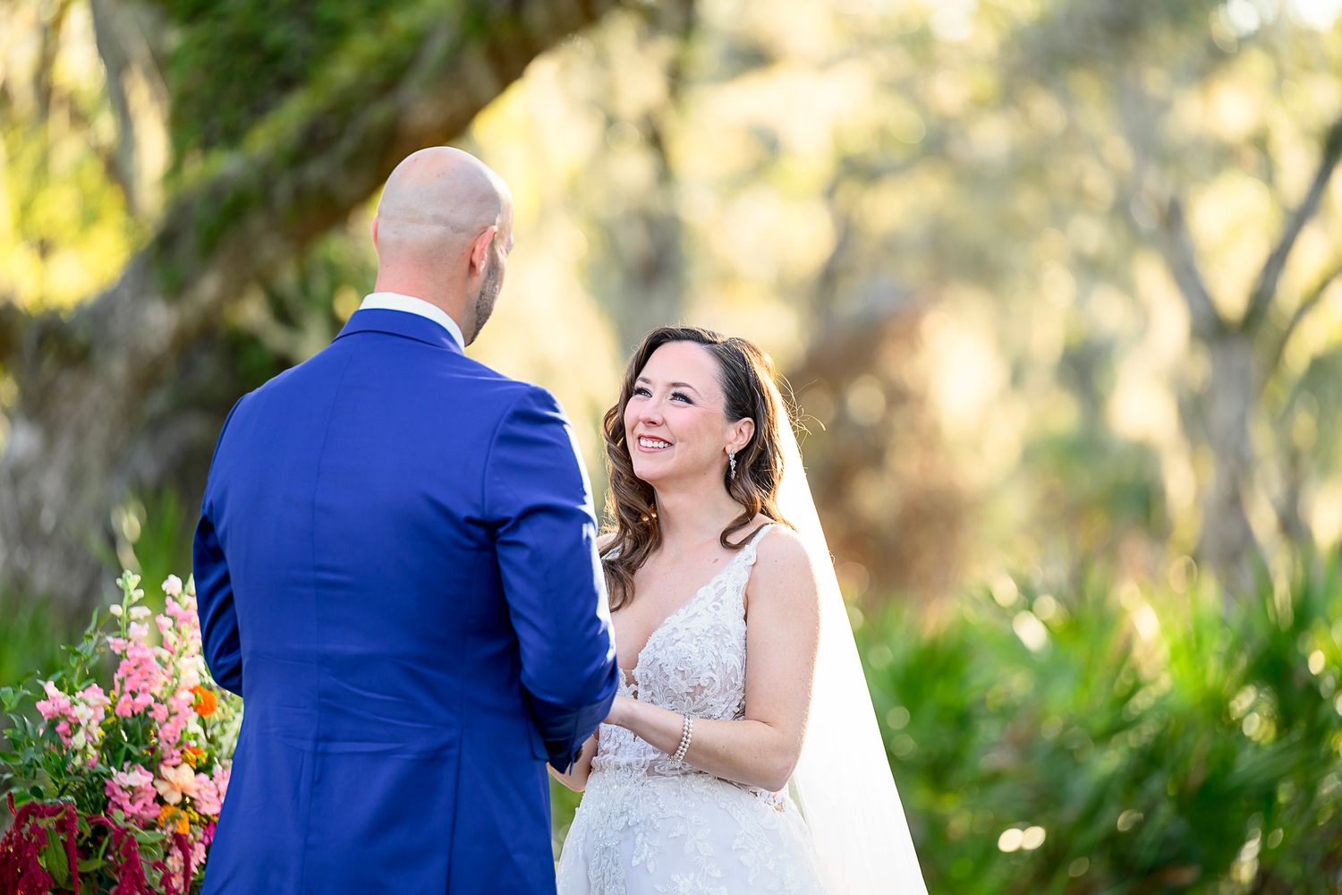 A couple shares a joyful moment during their outdoor garden wedding ceremony with colorful flowers in the background.
