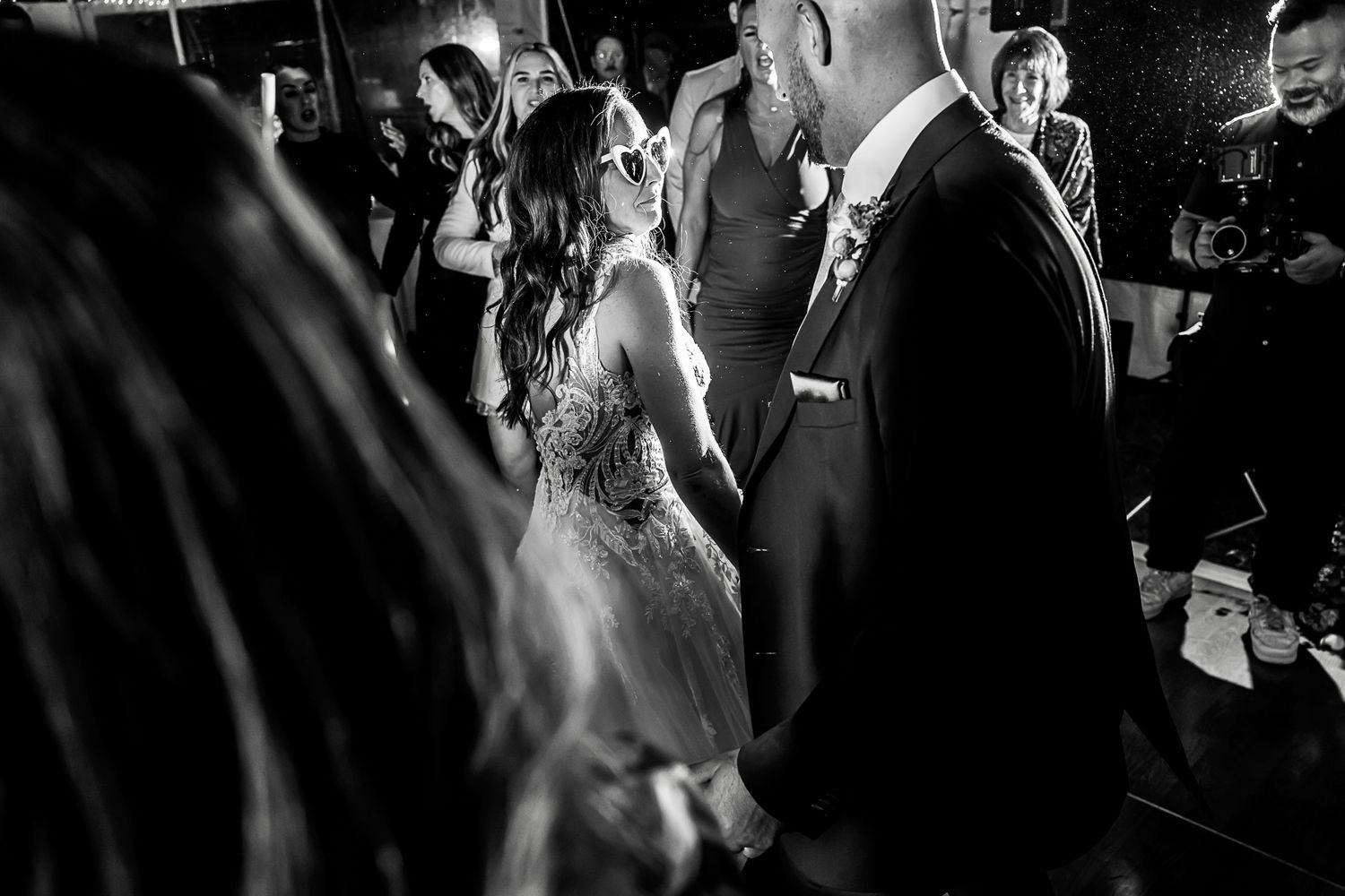 Black and white photo of couple dancing together at their wedding reception with guests looking on.
