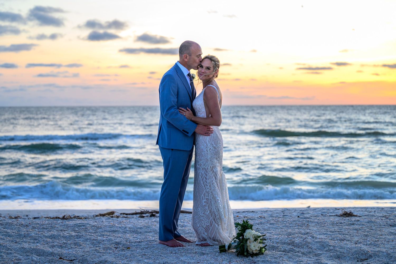 Romantic couple embracing on beach during sunset with ocean waves in background.