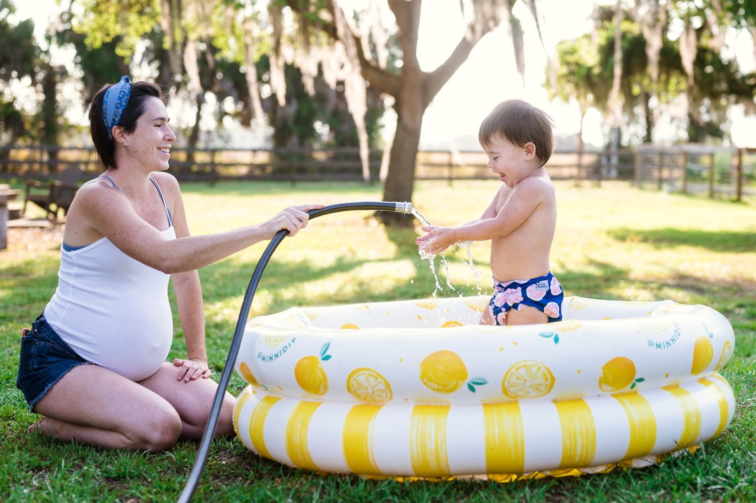 A yellow and white striped inflatable kiddie pool sits on grass in a sunny backyard setting.