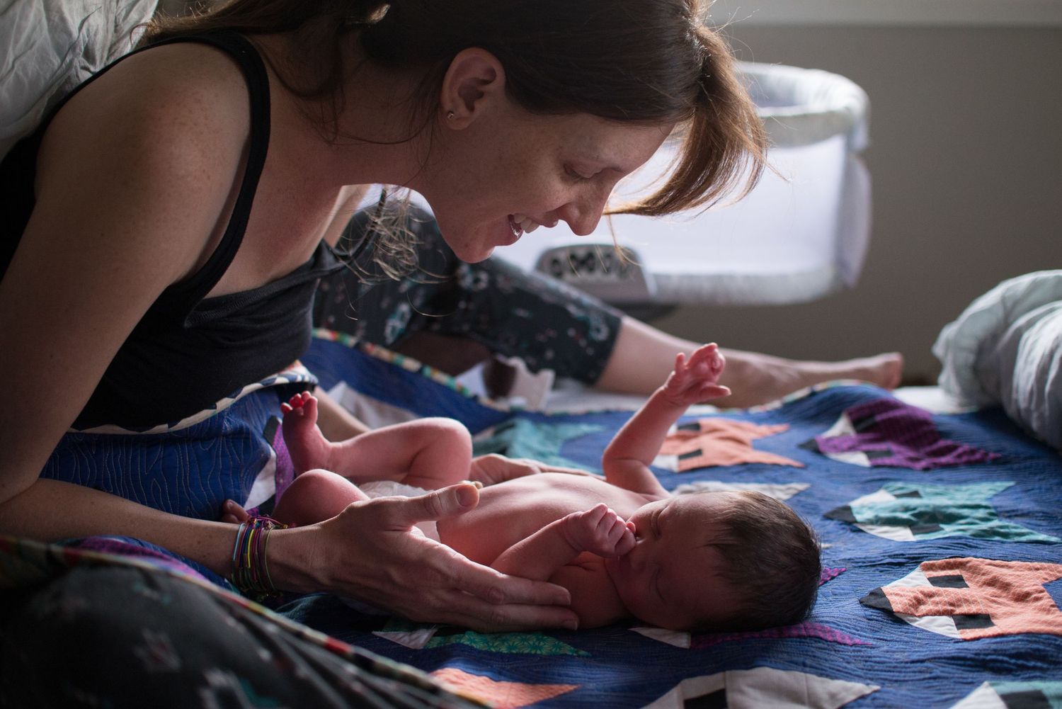 A baby lies on a colorful quilt while someone's hands gently touch their head and body during a massage session.