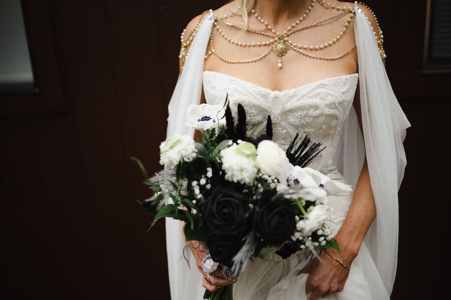Bride holding elegant black and white wedding bouquet with roses and baby's breath, wearing pearl necklace.