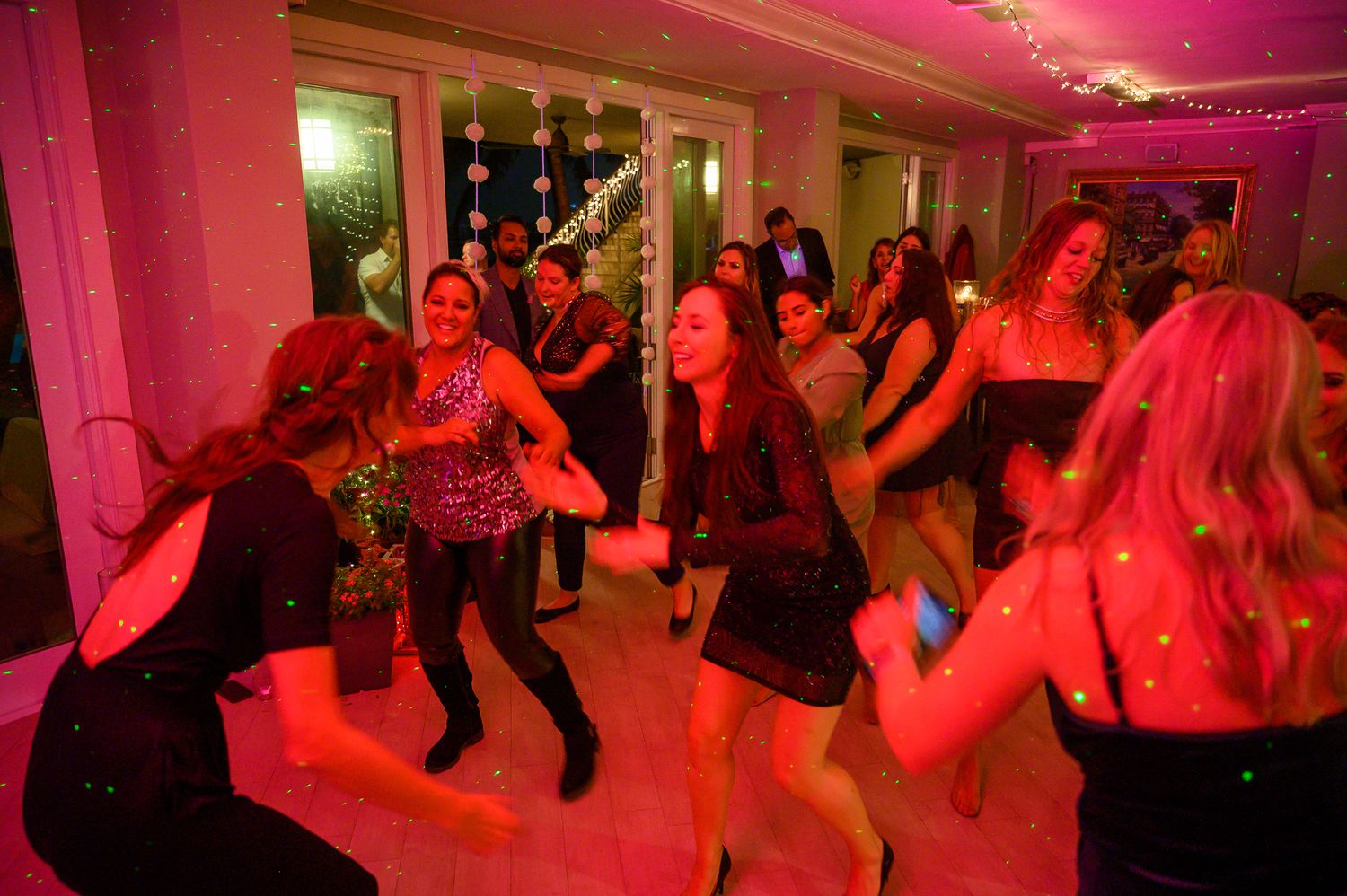 Party guests dance under vibrant red lighting at an indoor celebration.