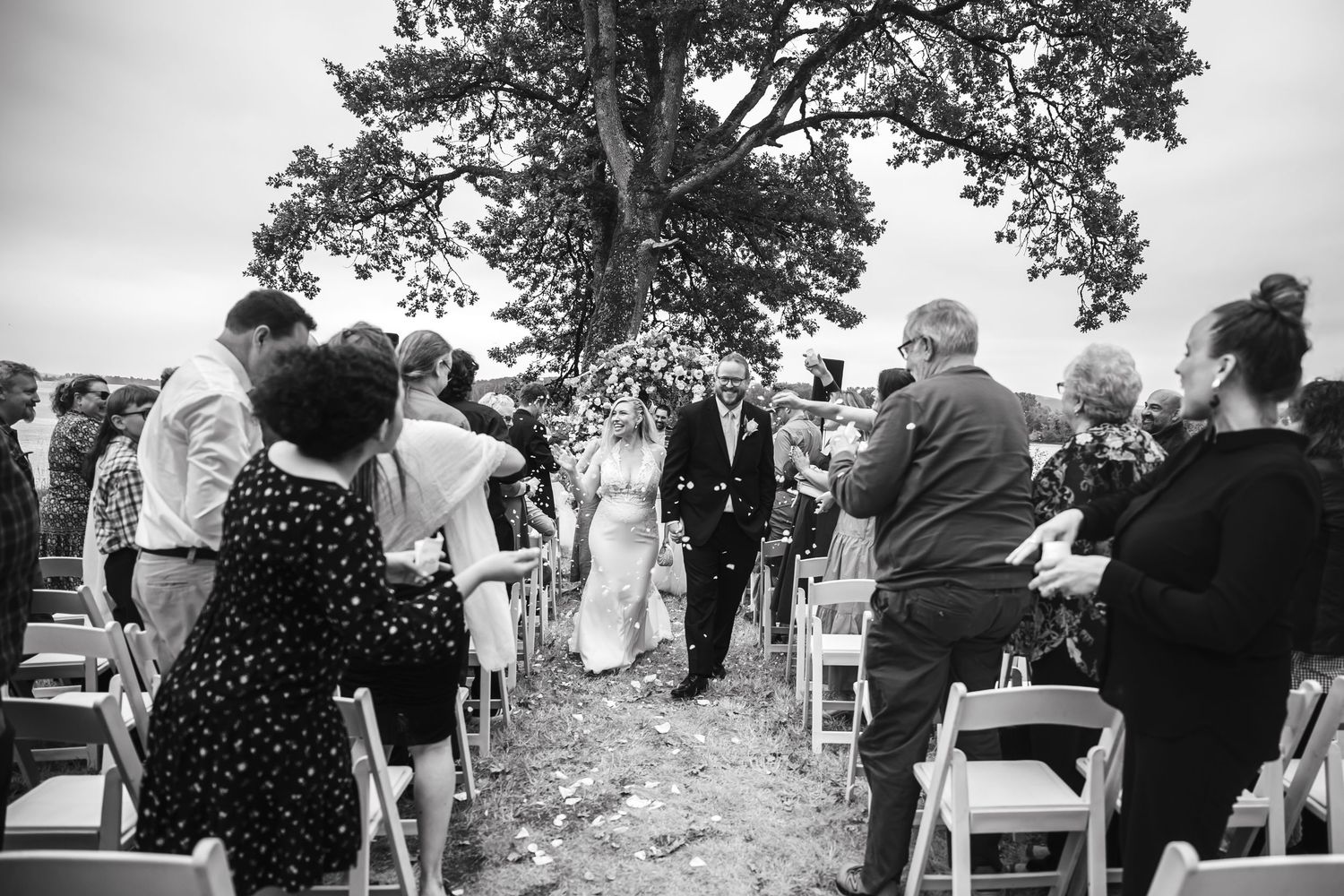 Outdoor wedding ceremony setup with white chairs arranged under tall trees.