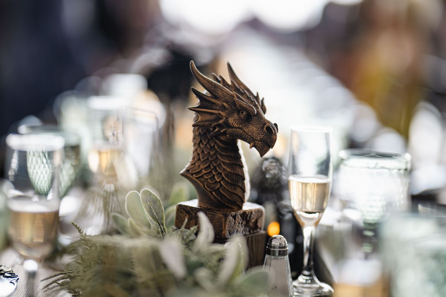 Decorative dragon figurine centerpiece surrounded by glassware and greenery at a wedding reception.