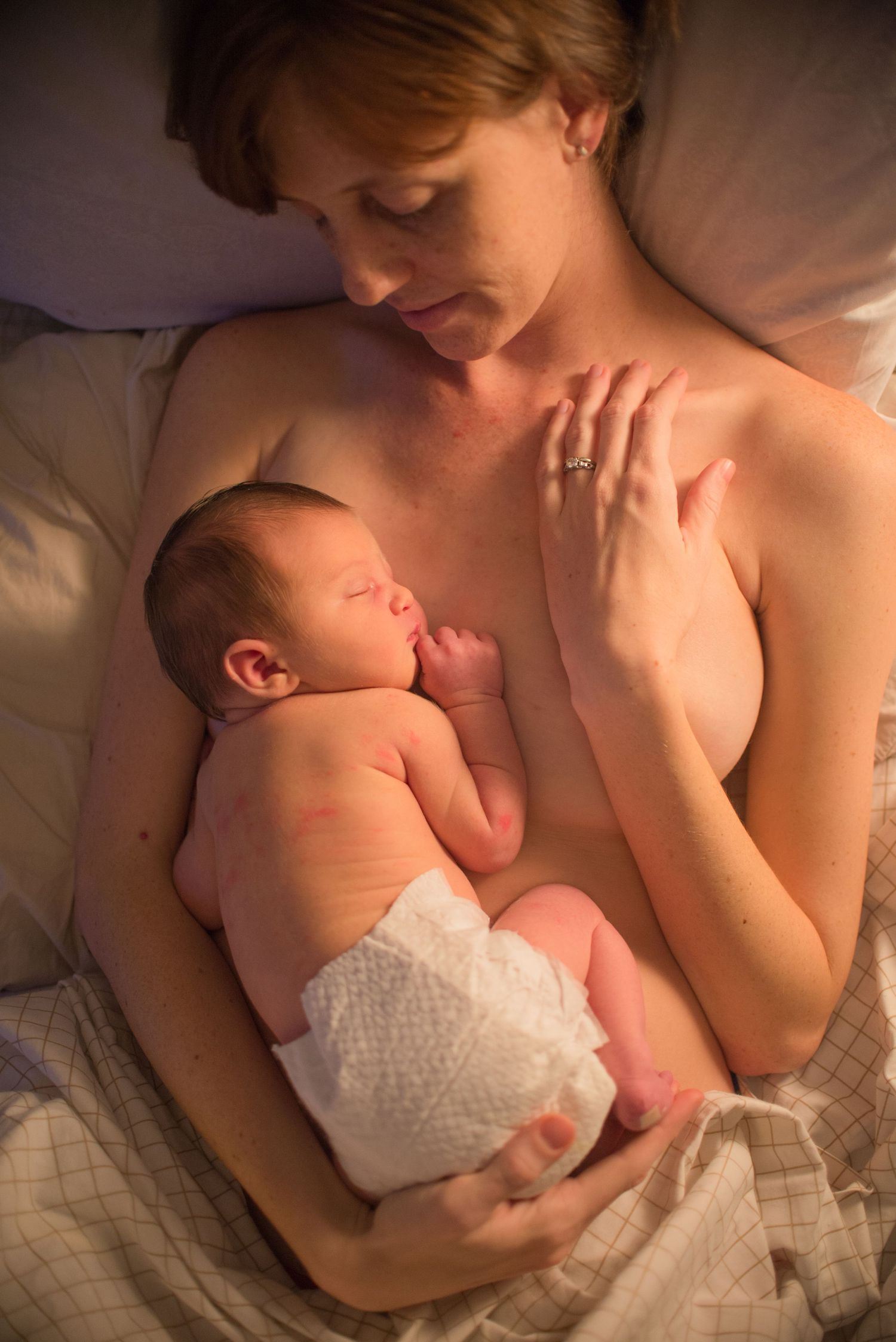 A tender moment between parent and newborn baby lying together in soft lighting on white bedding.