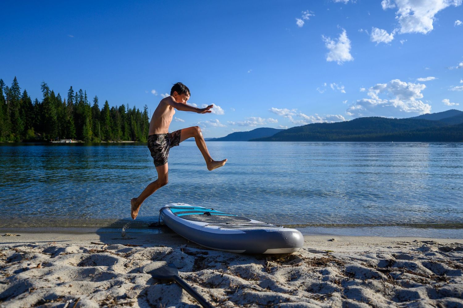 A sequence of action shots showing someone jumping into a lake from an inflatable paddleboard on a sunny summer day.