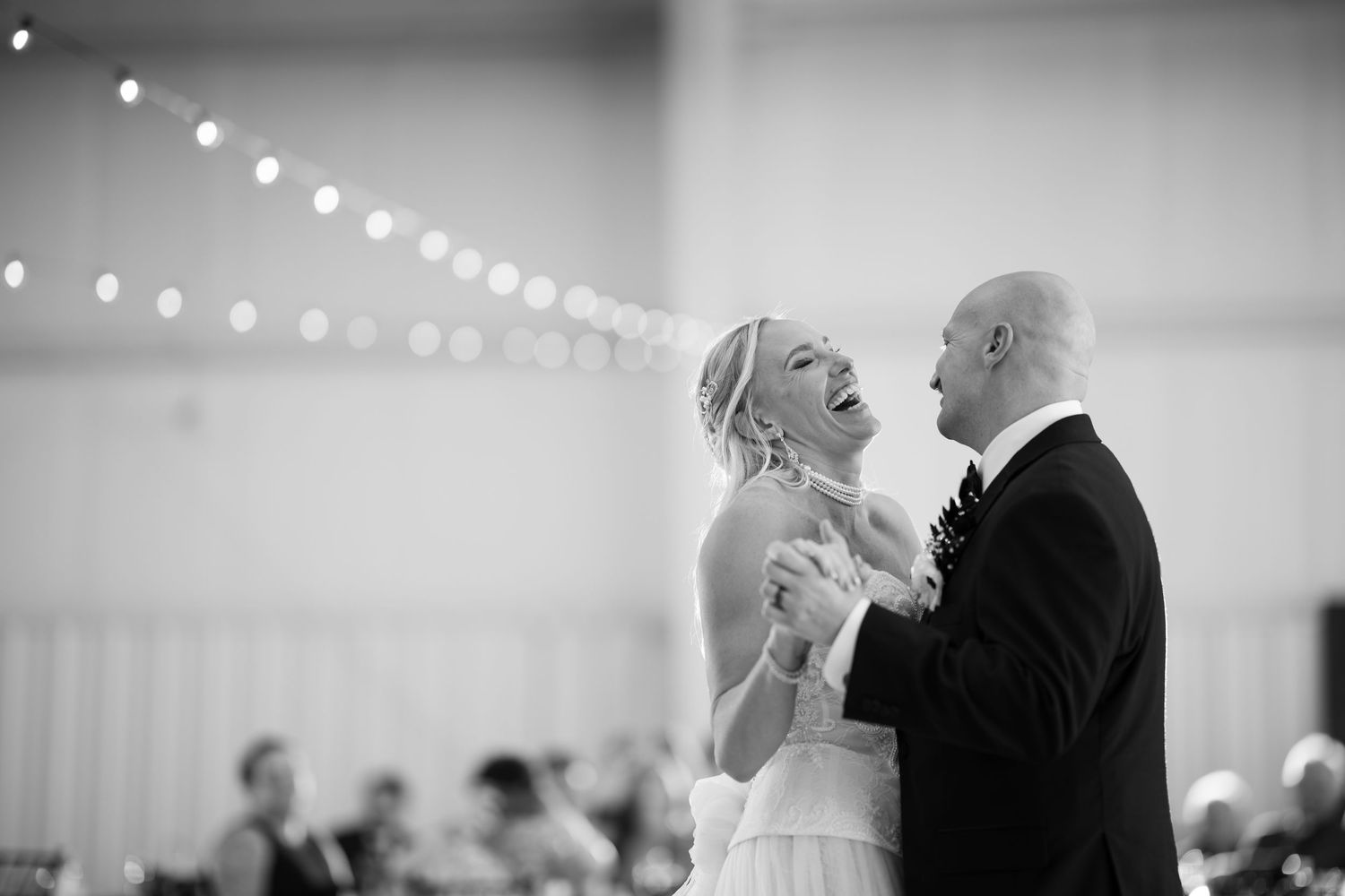 Black and white photo of a bride and groom sharing a joyful first dance at their wedding reception.