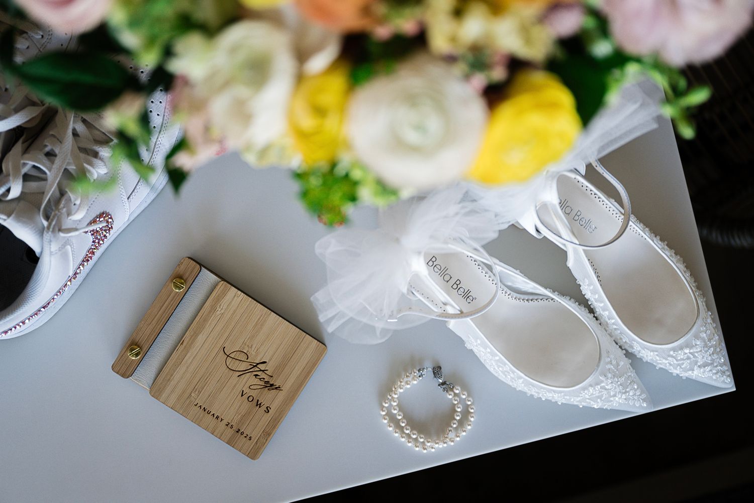 Wedding accessories including white shoes, rings, and a wooden box displayed alongside fresh flowers.