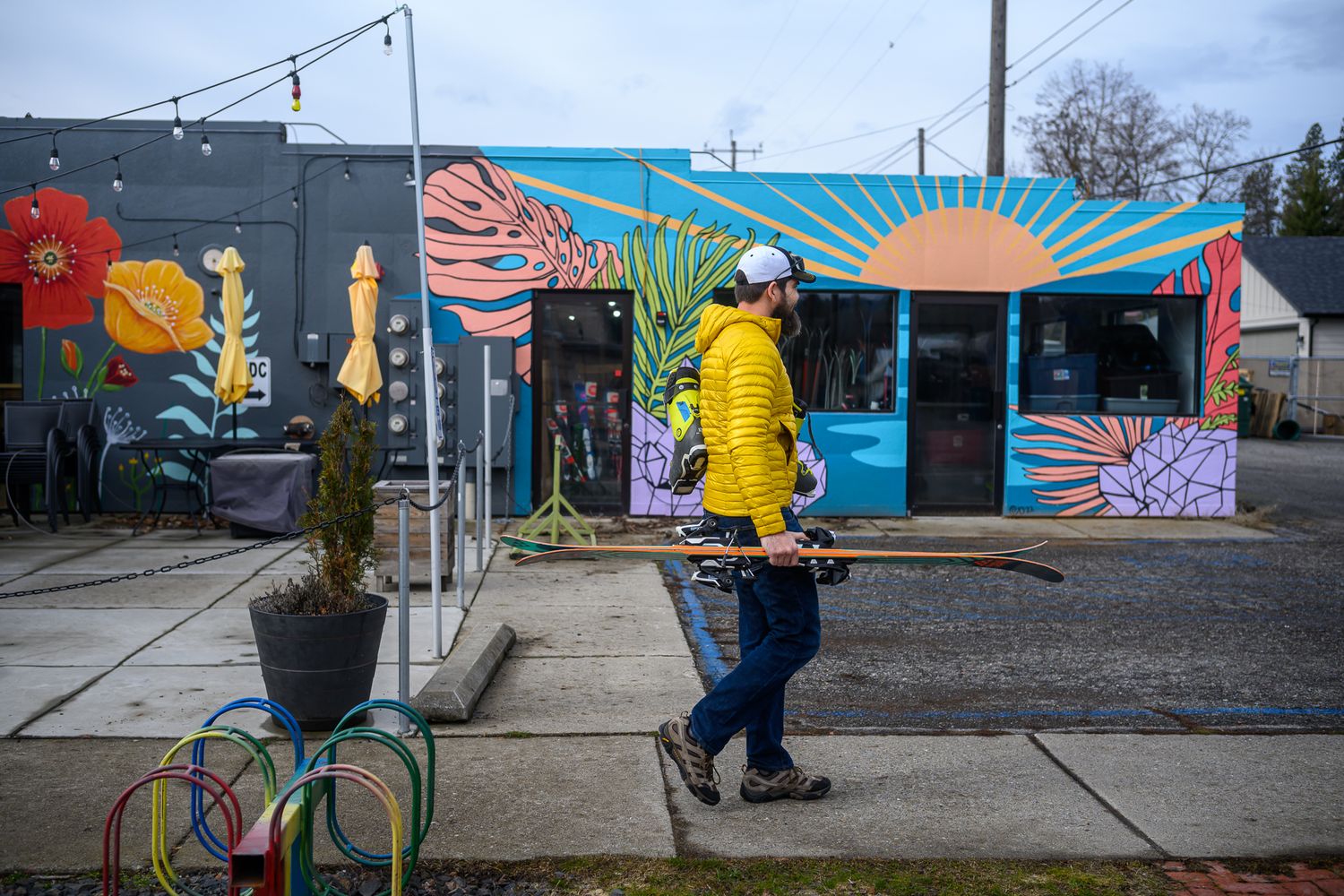 Person in yellow raincoat walking past colorful street art mural on urban building.