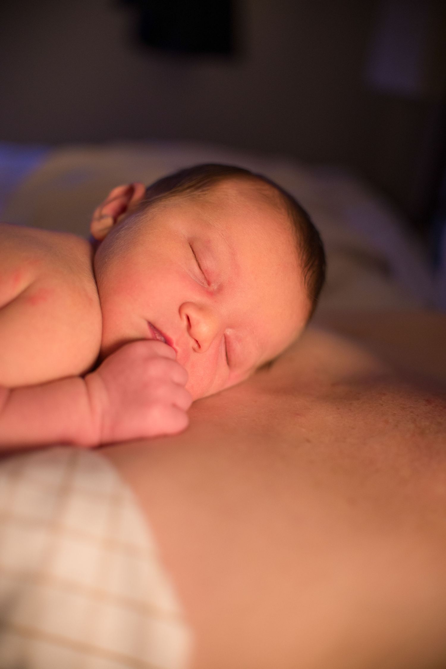A sleeping baby lies peacefully on a soft surface in warm lighting.
