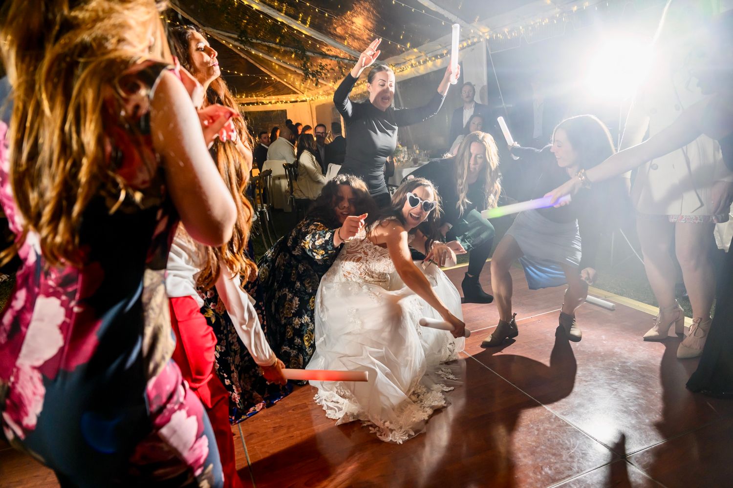 Wedding guests dancing in a lively crowd on a dimly lit dancefloor during an energetic reception celebration.