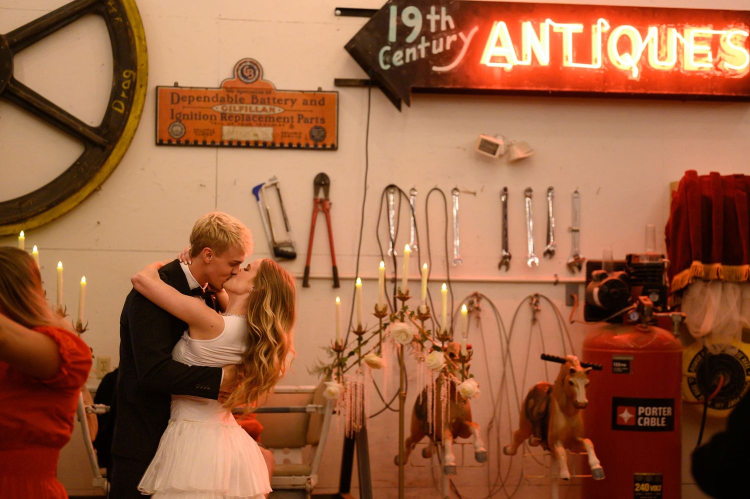 Couple shares first dance kiss in rustic antique shop with vintage tools and glowing 19th Century Antiques sign.