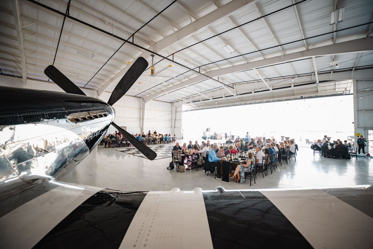 Wedding reception held inside a spacious aircraft hangar with vintage propeller plane on display.