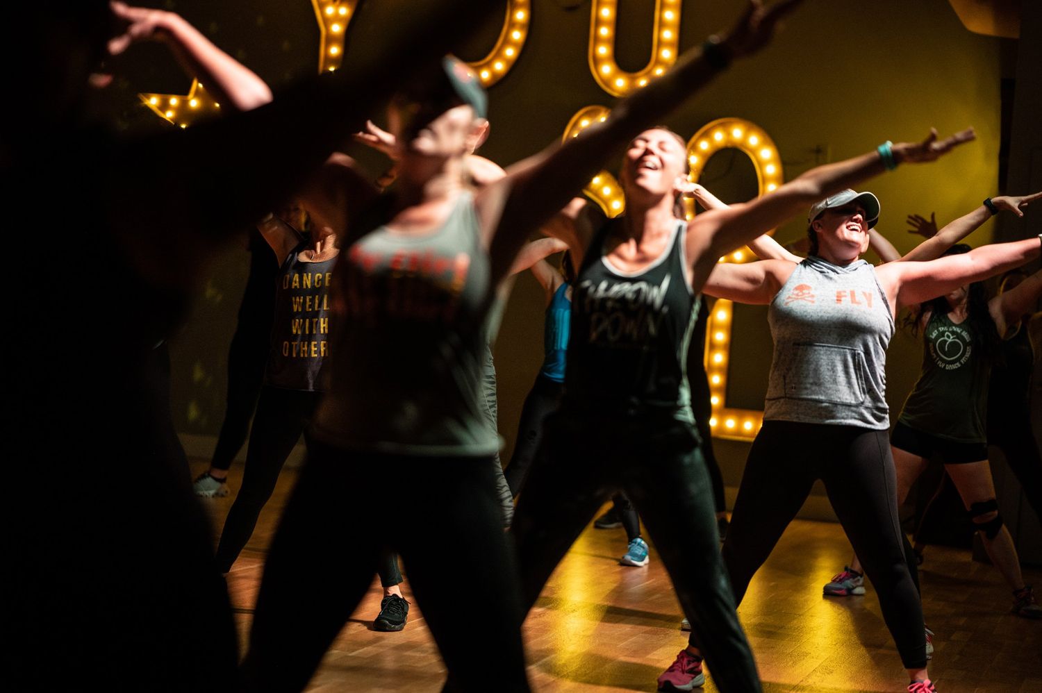 Dancers perform an energetic choreographed routine in a dark studio with glowing lights in the background.