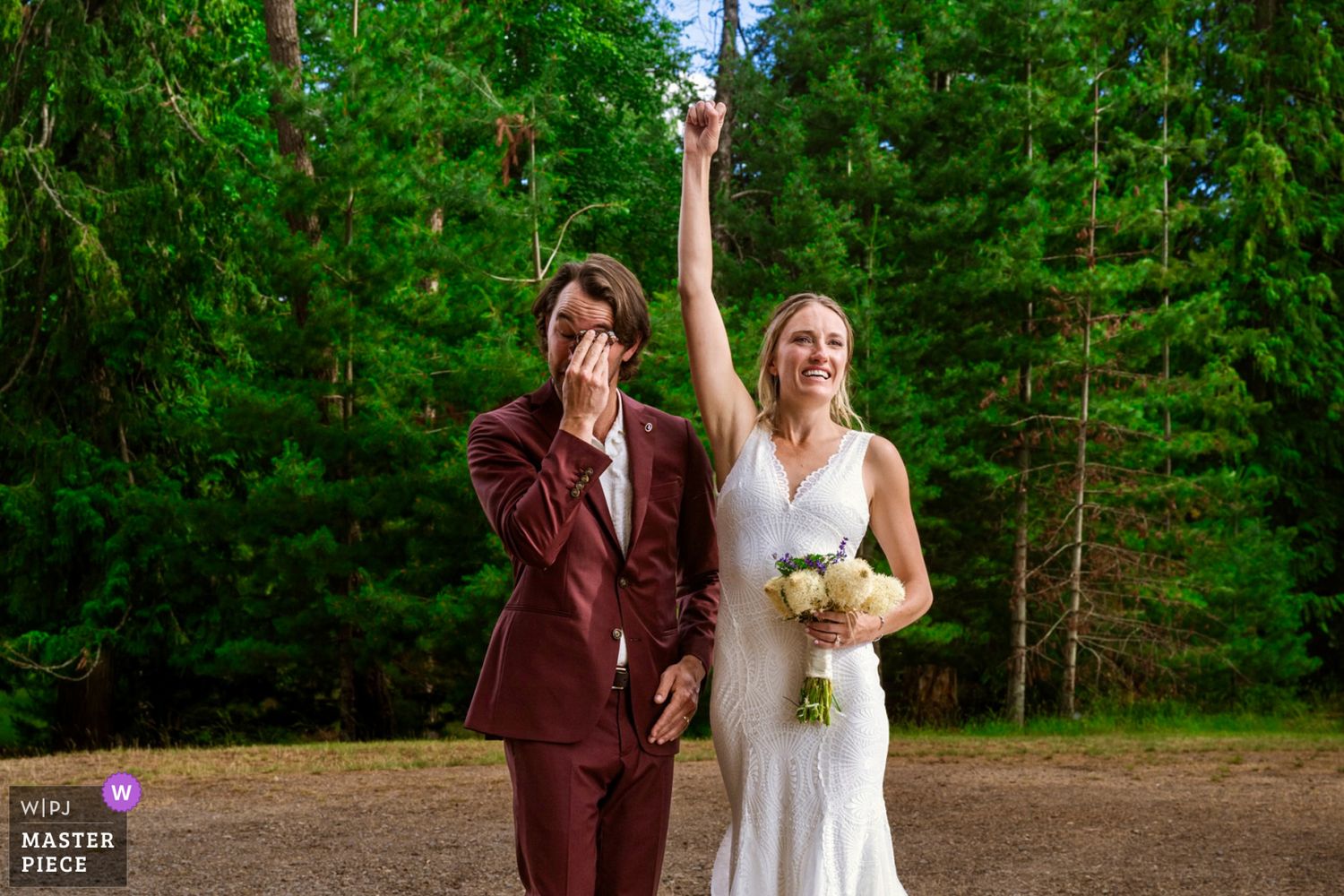 Two people in wedding attire stand together in front of evergreen trees during an outdoor forest ceremony WPJA 2025 ranked #8 wedding photo