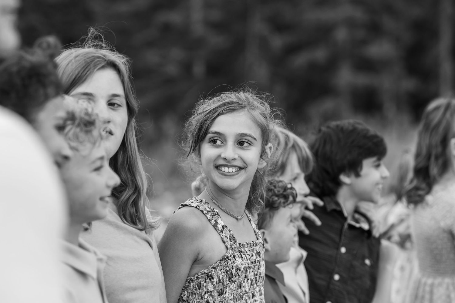 Black and white photo of smiling children gathered outdoors at a casual event.