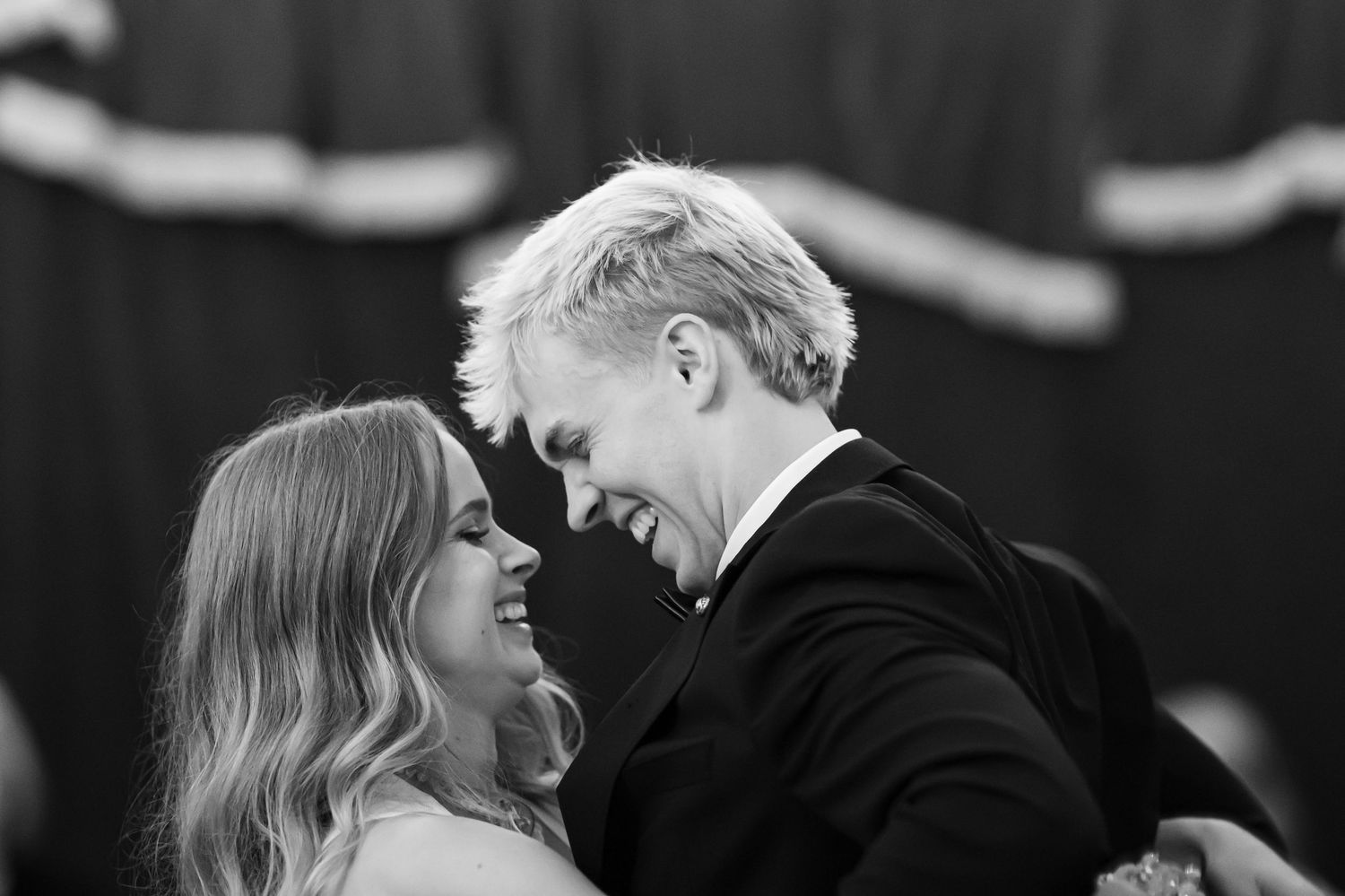 Bride and blonde groom share a joyful laugh during their first dance in black and white wedding photo.
